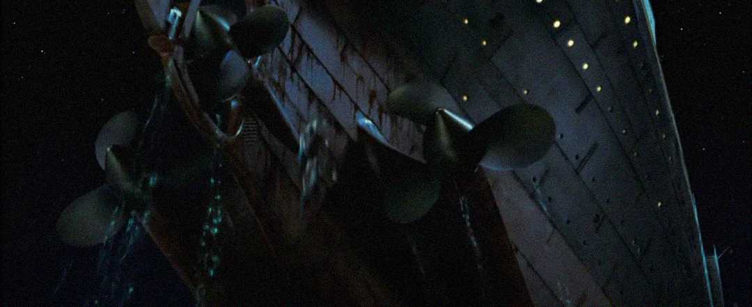 View from below a large ship’s stern at night, showing massive propellers partly out of water and the hull illuminated by small lights, with water cascading down.