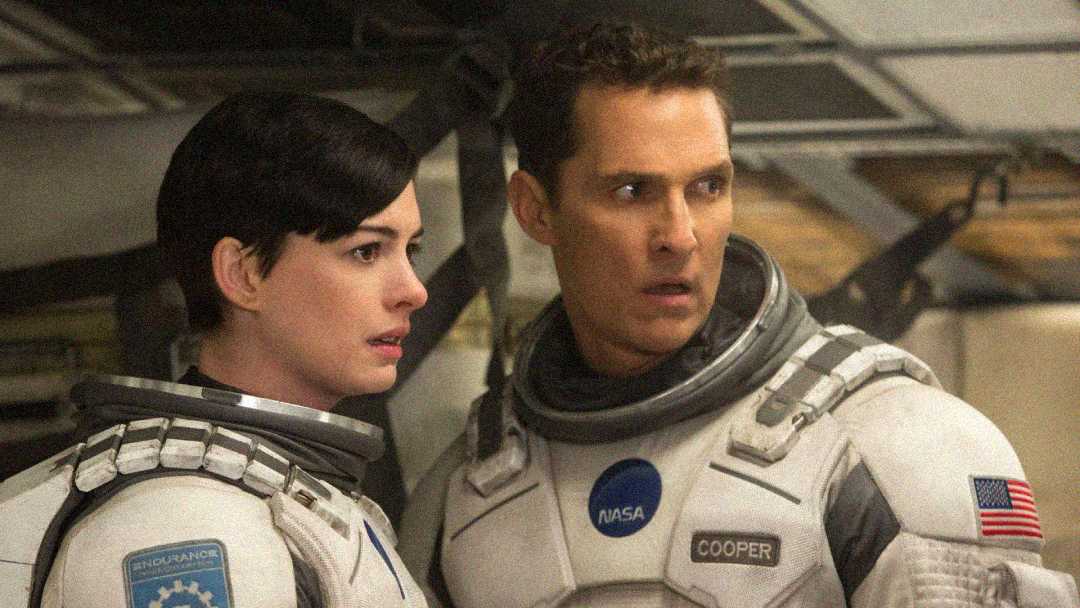Two astronauts in white space suits with NASA logos stand close together, looking intensely at something off-camera. The background suggests the interior of a spacecraft or station.