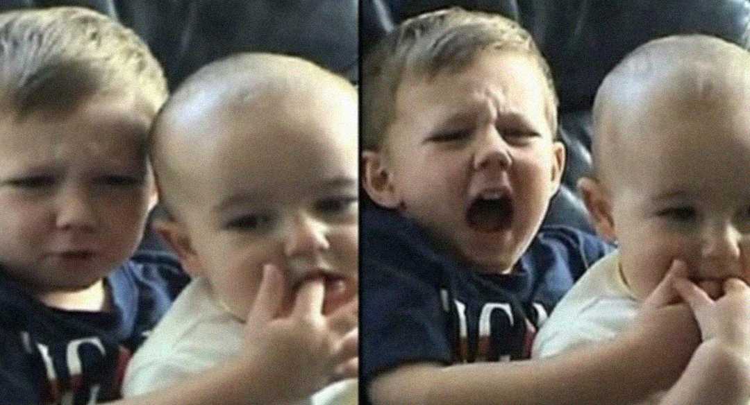 Two young children sit together. In the first frame, the smaller child puts their finger in the older child’s mouth. In the second frame, the older child reacts in pain as the baby’s finger is still in their mouth.