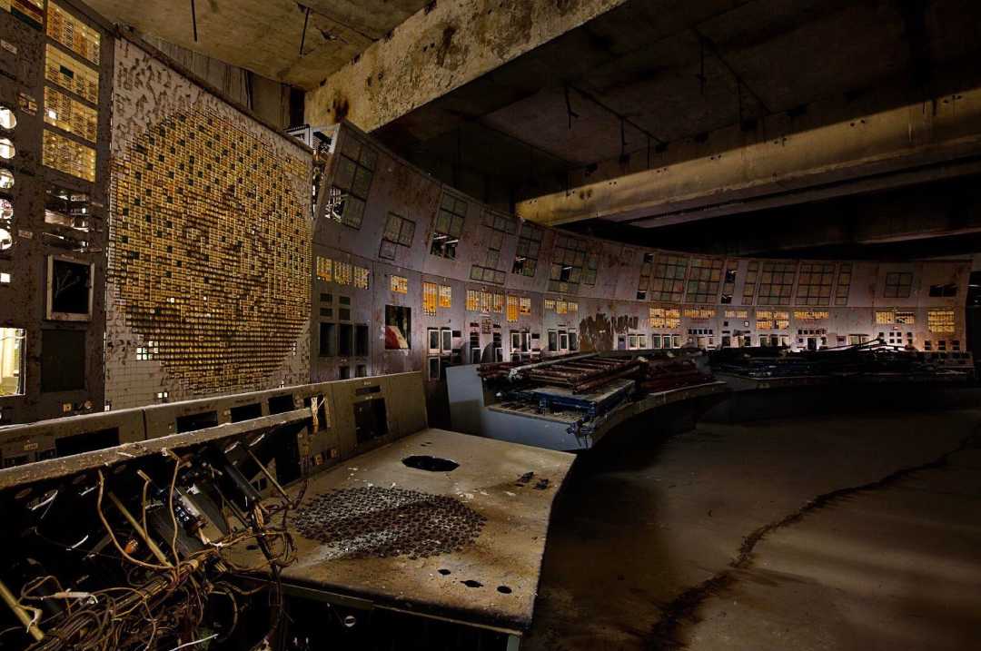 An abandoned, dimly lit control room with rusty panels, broken buttons, exposed wires, and decaying desks. The walls are lined with old, illuminated indicators and switches, giving the space a neglected, eerie atmosphere.