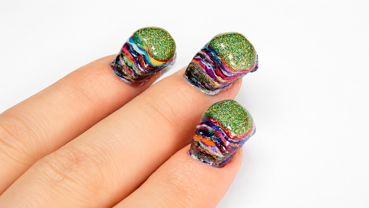 Three fingers with thick, chunky nail polish featuring layers of green glitter and colorful swirls, creating an unusual, textured look, against a plain white background.