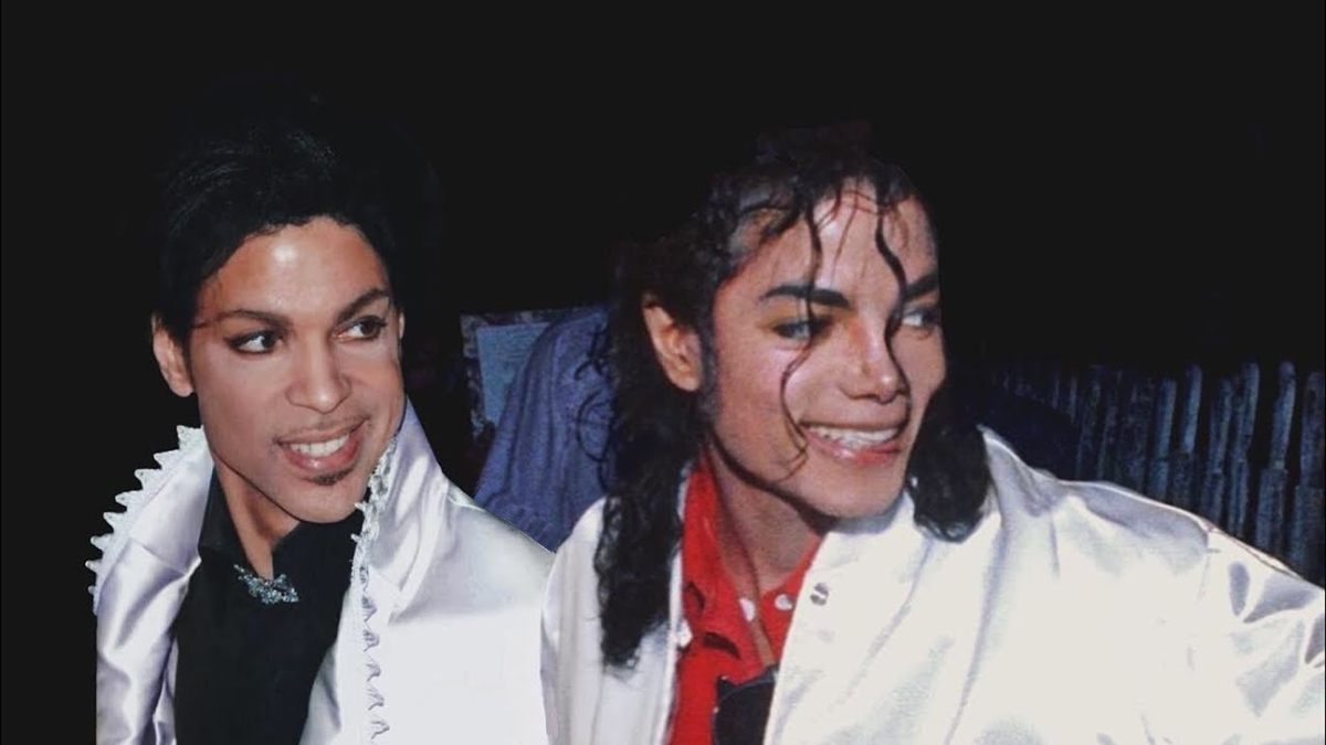 Two people wearing shiny white jackets smile while standing next to each other against a dark background.