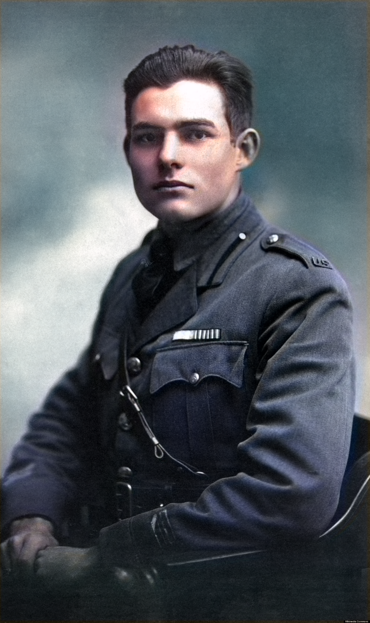 A young man in a military uniform sits for a formal portrait, looking directly at the camera. The photograph is colorized, with a soft, blurred background.