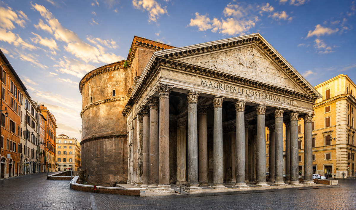 The Pantheon in Rome, Italy, stands under a blue sky with clouds. Its ancient columns and dome are highlighted by warm sunlight. Surrounding buildings line the cobblestone square, which appears empty.