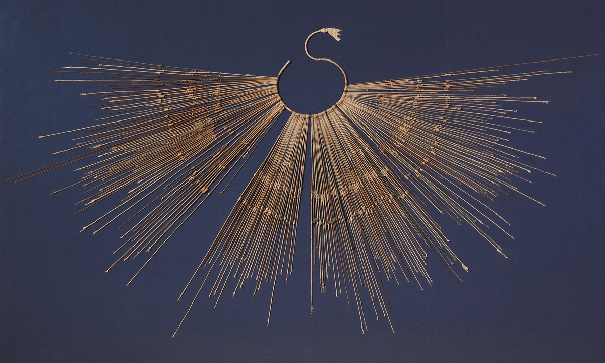 A circular structure with radiating strings, resembling a sunburst or abstract fan, set against a dark blue background.