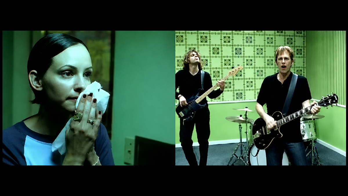A split-screen image shows a woman holding a tissue to her mouth on the left, and a three-member band playing guitar, bass, and drums in a green room with patterned wallpaper on the right.