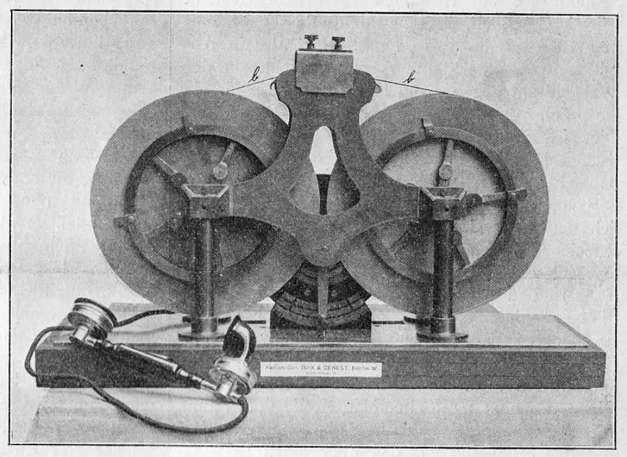 A vintage scientific device with two large metal disks, a central structure connecting them, and attached wires leading to a pair of old-fashioned headphones on the left.