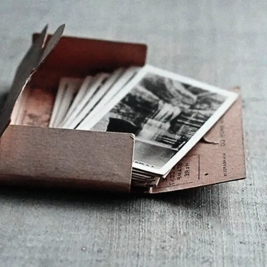 A brown envelope lies open on a gray surface, revealing a stack of black-and-white photographs partially visible inside.