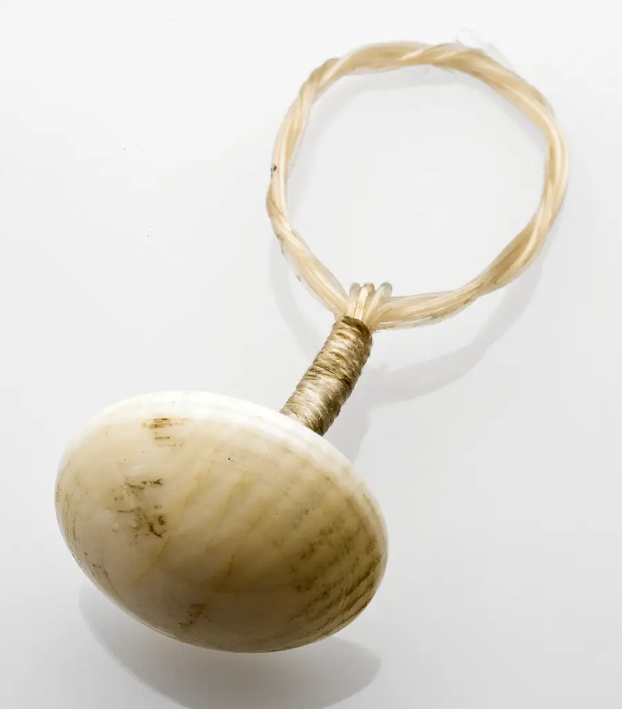 A close-up of a traditional Hawaiian fishhook made from a shell and fiber cord, set against a white background.