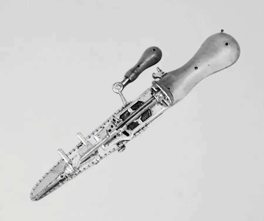 A black and white photo of an antique surgical tool with a handle and a serrated blade, resembling a small handheld saw, displayed against a plain background.