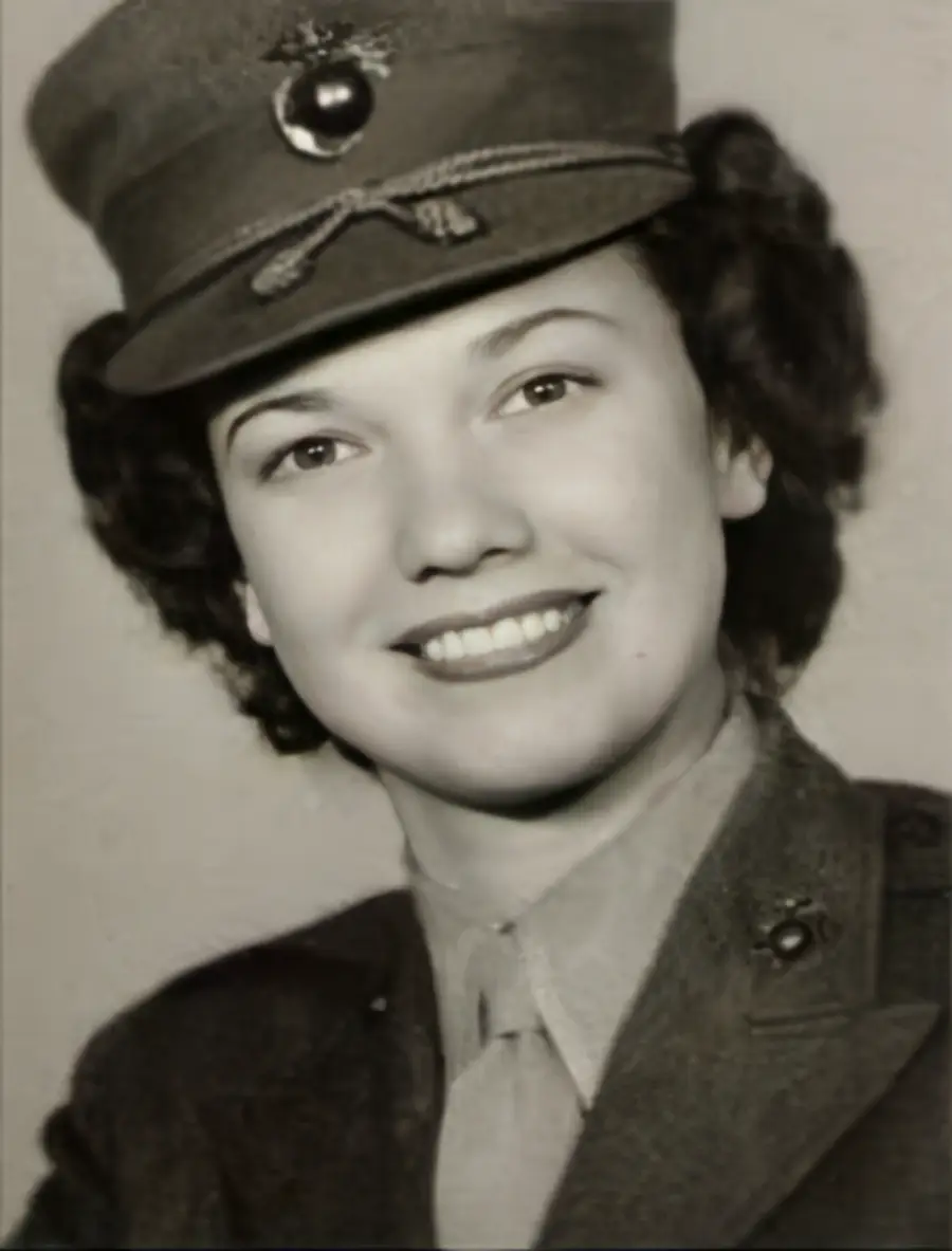 A woman in a military uniform and cap smiles at the camera in this black-and-white portrait.