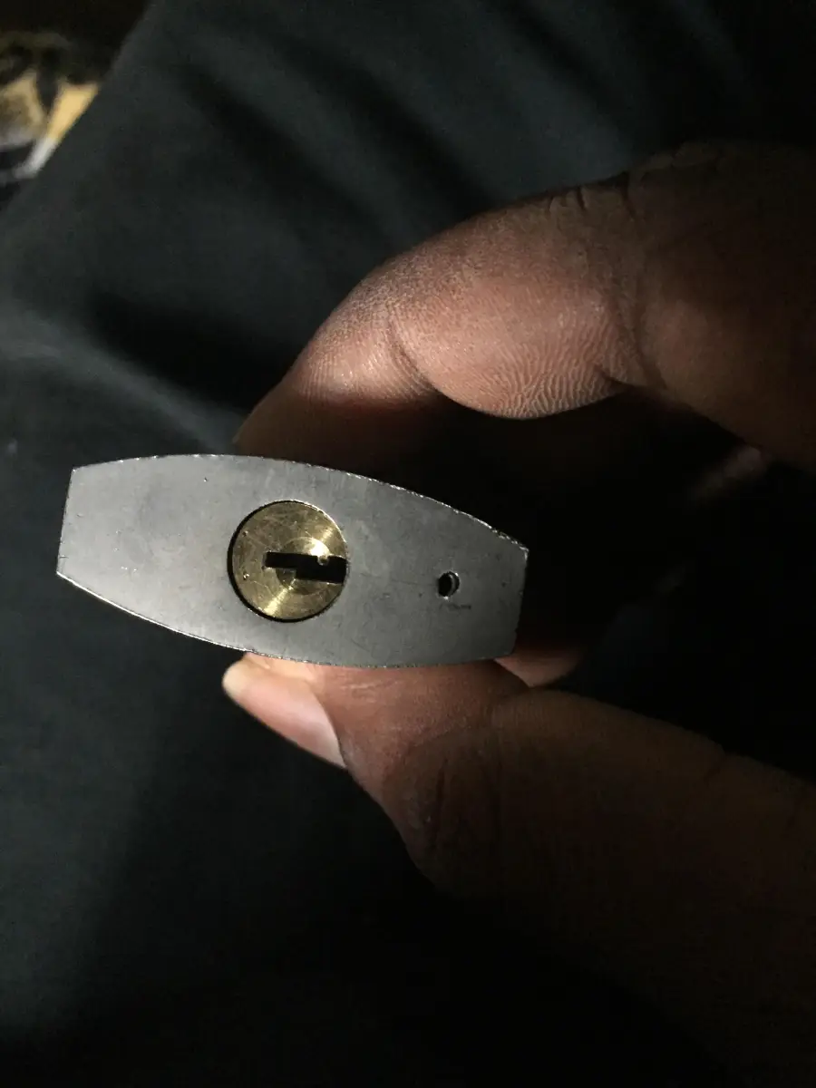 A close-up of a hand holding a silver padlock, showing the keyhole and lock mechanism against a dark background.