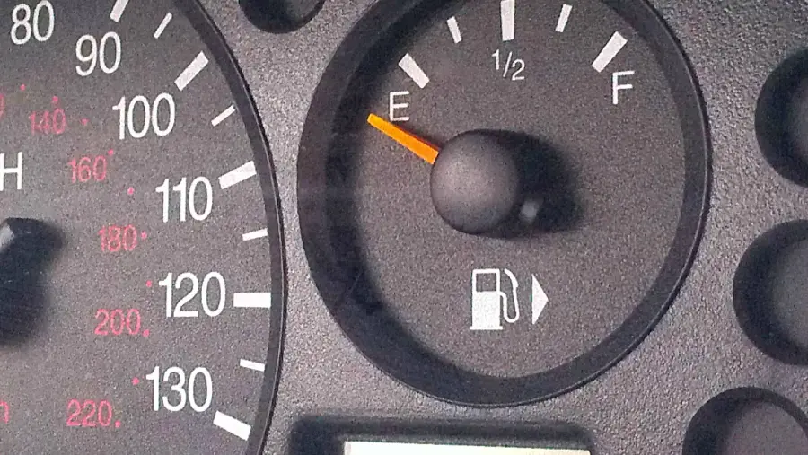 A car fuel gauge showing the needle pointing to empty, indicating that the fuel tank is nearly out of gas. Part of a speedometer is also visible to the left.