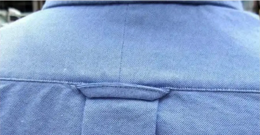 Close-up of the back of a blue collared shirt, focusing on a small horizontal fabric loop located just below the yoke seam.