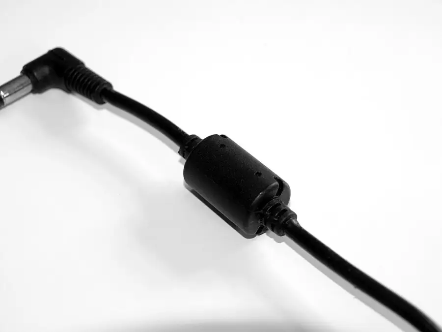 A close-up of a black power cable with a right-angle connector and a cylindrical ferrite bead in the middle, set against a white background.