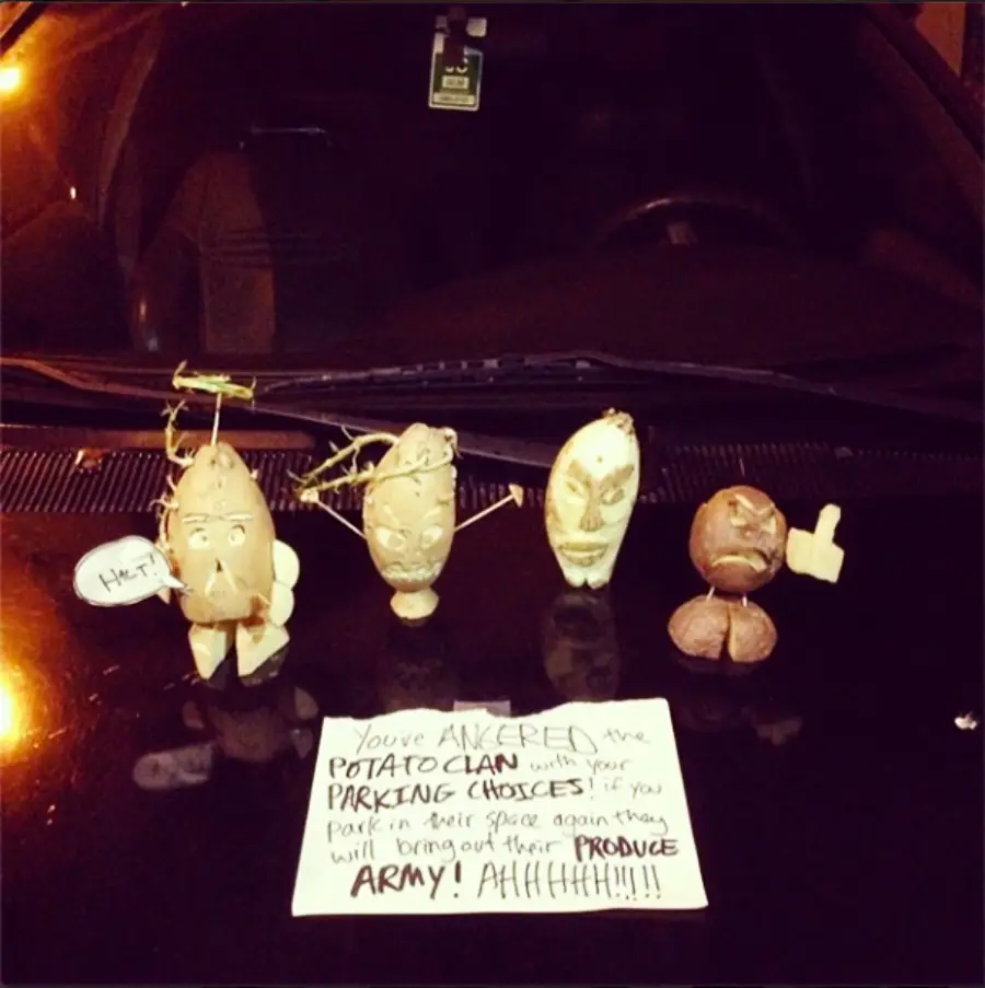 Four decorated potatoes with faces and props stand on a car hood with a note warning about parking choices, saying the "potato clan" will bring out their "produce army" if it happens again.