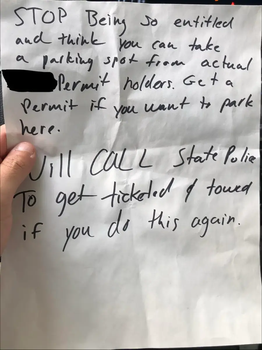 A handwritten note warns someone not to park in a permit spot, stating to get a permit or risk being ticketed and towed, with "CALL" written in large letters. A person's hand holds the paper.