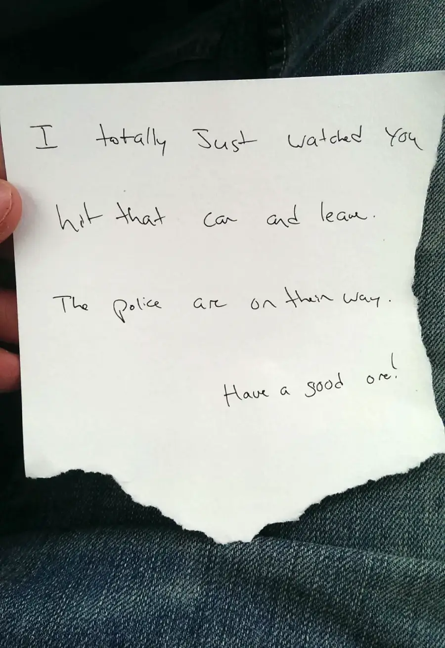 A handwritten note on torn paper reads: "I totally just watched you hit that car and leave. The police are on their way. Have a good one!" It rests on someone's jeans.