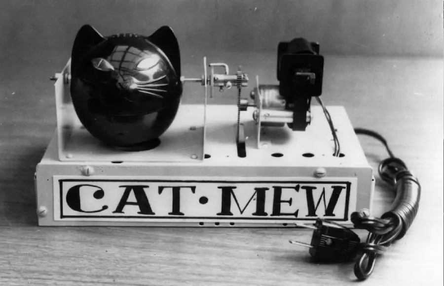 A vintage device labeled "CAT MEW" with a cat-shaped head and electrical components, including a power cord and plug, on a flat surface.