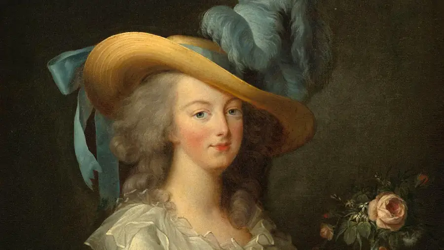 A woman in an 18th-century dress and wide-brimmed hat with blue feathers holds flowers, posing against a dark background.