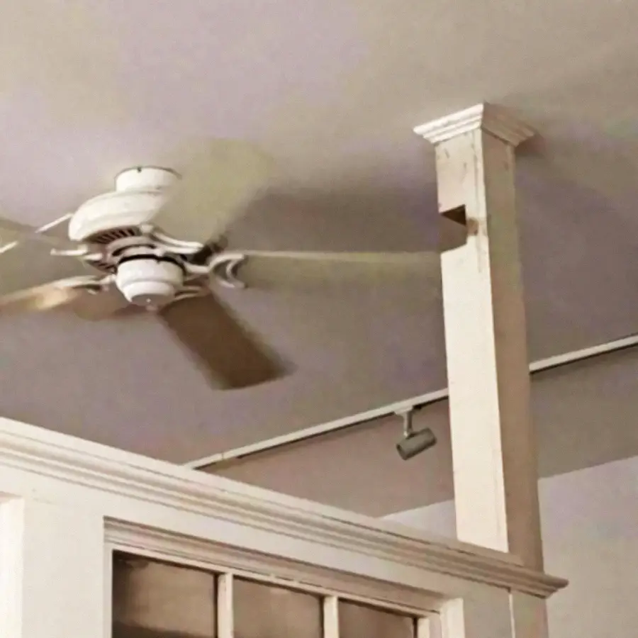 A spinning ceiling fan is very close to a supporting beam, making it look like it could hit the beam as it rotates.