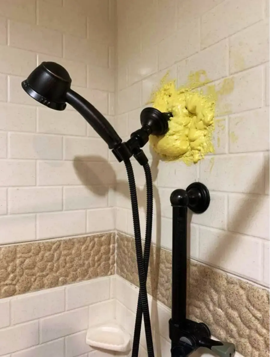 A showerhead is attached to a wall with a large, messy clump of yellow foam sealant instead of a proper fixture or bracket.