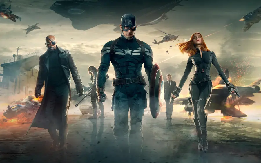 Three superheroes in action poses walk forward amid debris, jets, and smoke, with two other figures in the background. The central hero holds a shield, flanked by a man in a coat and a woman in a black suit.