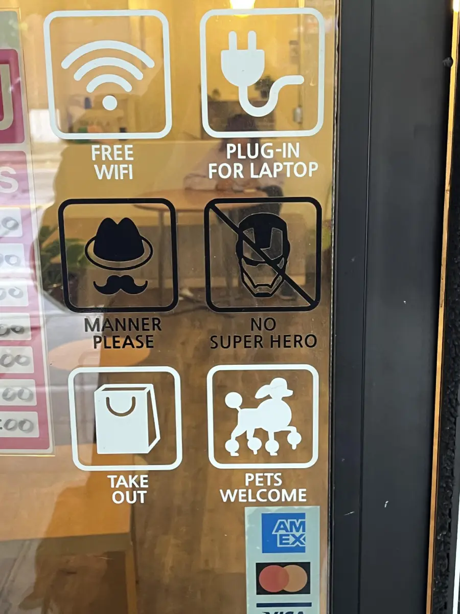 A glass door displays icons indicating free WiFi, plug-in for laptops, "manner please," "no superhero," take out available, pets welcome, and acceptance of American Express.