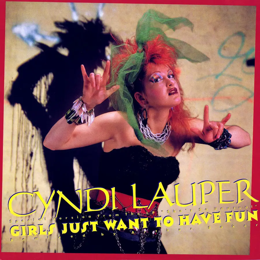 Cyndi Lauper poses with colorful hair, bold makeup, and funky accessories, making hand gestures. The text reads "Girls Just Want to Have Fun." The background is yellow with a red border.