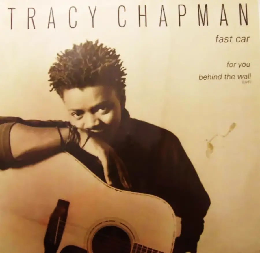 Album cover with person holding an acoustic guitar, looking at the camera. Text at the top reads “Tracy Chapman.” Other text lists “Fast Car,” “For You,” and “Behind the Wall (Live).” Background is beige.