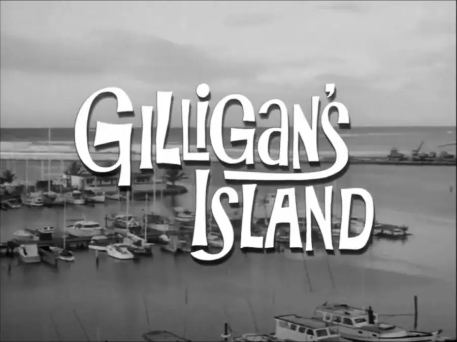 Black-and-white image of a marina with several docked boats. Large stylized text over the scene reads “Gilligan’s Island.” The ocean and cloudy sky are visible in the background.