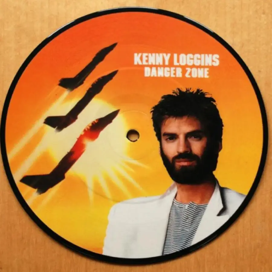A vinyl record features Kenny Loggins’ portrait, three fighter jets, and the text “KENNY LOGGINS DANGER ZONE” on an orange background.