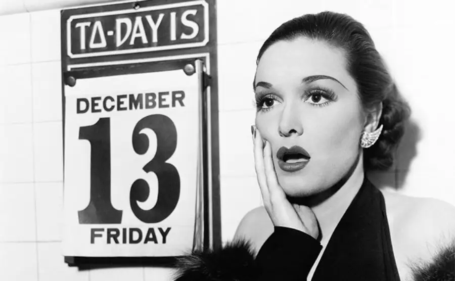 A surprised woman stands next to a wall calendar displaying "Today is Friday, December 13." She holds her cheek with one hand, conveying shock or worry about the date.