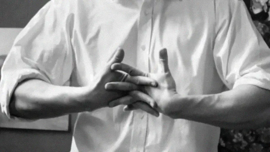 A person in a white button-up shirt cracks their knuckles by interlacing their fingers.