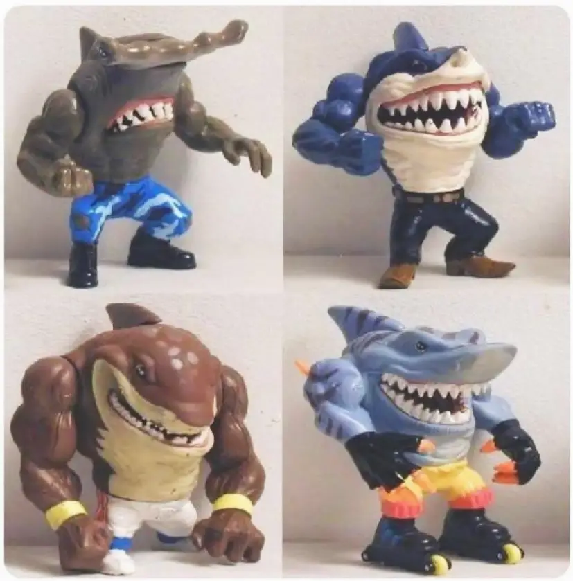 Four action figures resembling muscular, anthropomorphic sharks with sharp teeth are posed in dynamic stances. Each has a distinct shark species head and wears different colored pants and accessories.