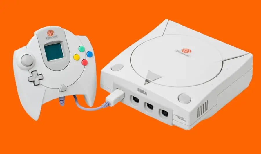 A white Sega Dreamcast console with a matching controller is displayed against a solid orange background. The controller is plugged into the console and features colorful buttons and a small screen.