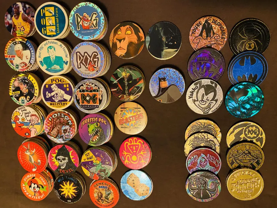 A collection of colorful POG milk caps featuring various characters, logos, and designs, neatly arranged in rows on a dark surface.