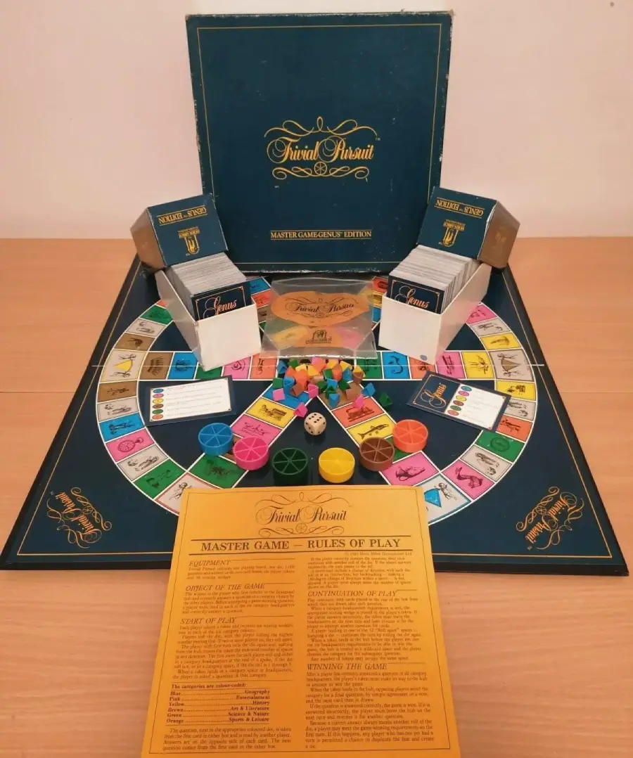 Trivial Pursuit board game set up with game board, question cards in boxes, colored player tokens, wedges, dice, and the rule sheet, all displayed neatly on a wooden table.
