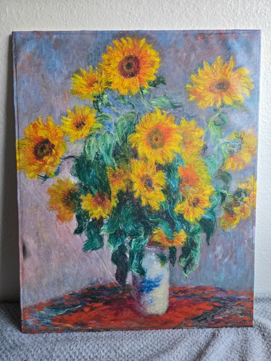 A painting of bright yellow sunflowers in a white vase with green leaves, set on a red cloth against a grayish background.