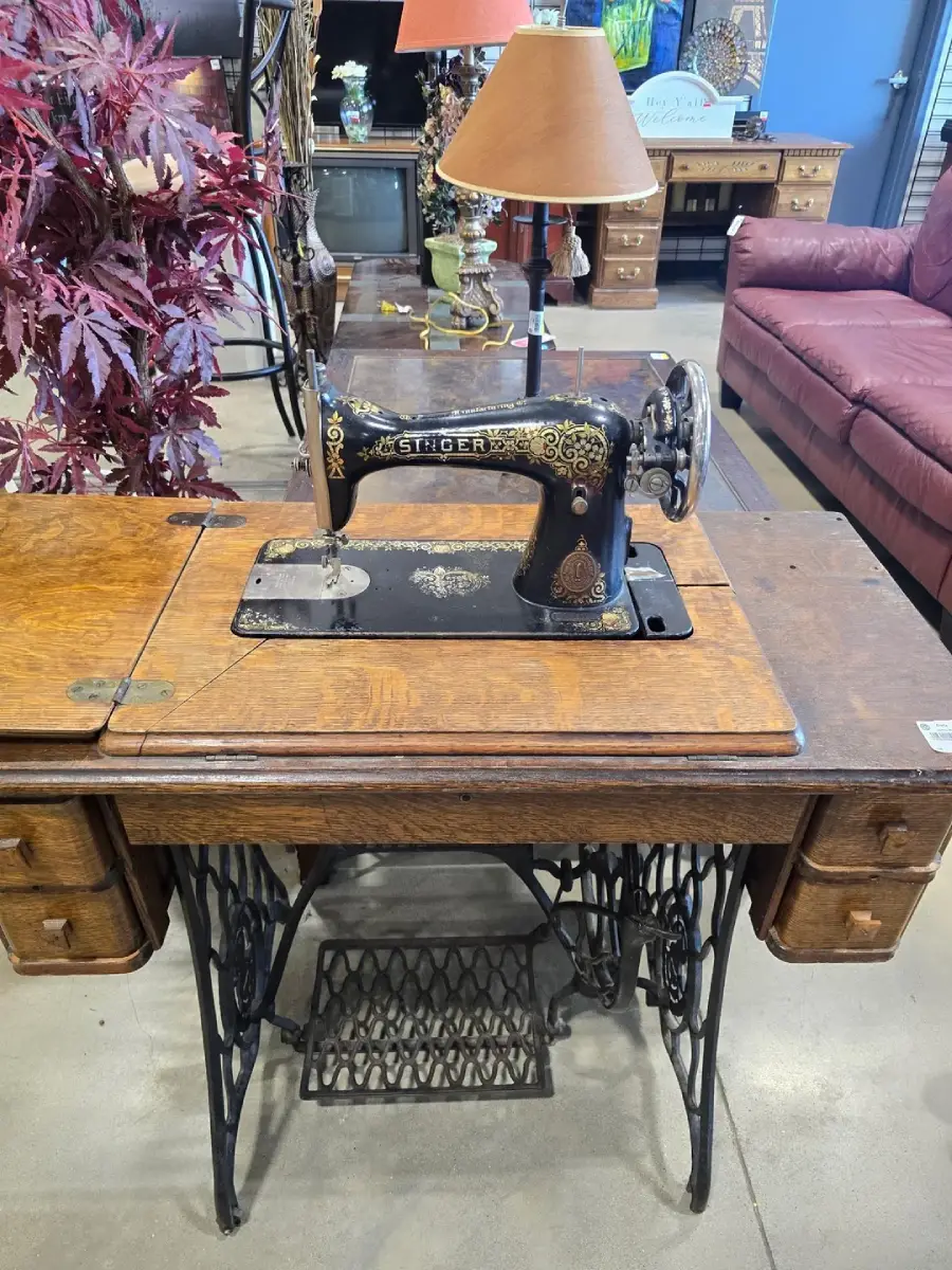 Antique black Singer sewing machine with gold detailing, set in a wooden cabinet with drawers, displayed indoors among other vintage furniture.