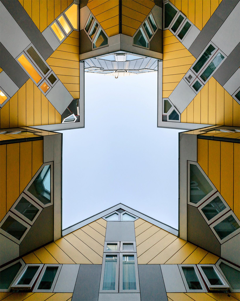 A view looking up at geometric, yellow and gray cube-shaped buildings with windows, forming a star-shaped opening to the sky.