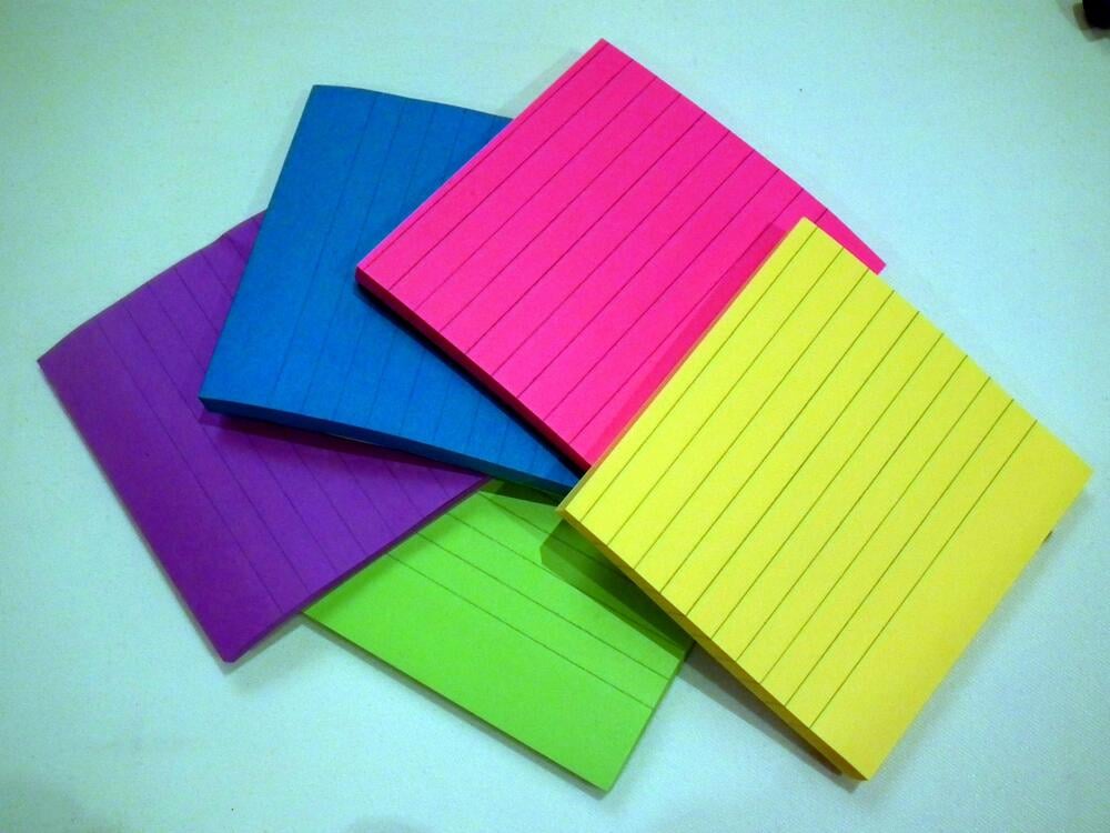 Five lined notepads in blue, pink, yellow, green, and purple, arranged in a fan shape on a white surface.