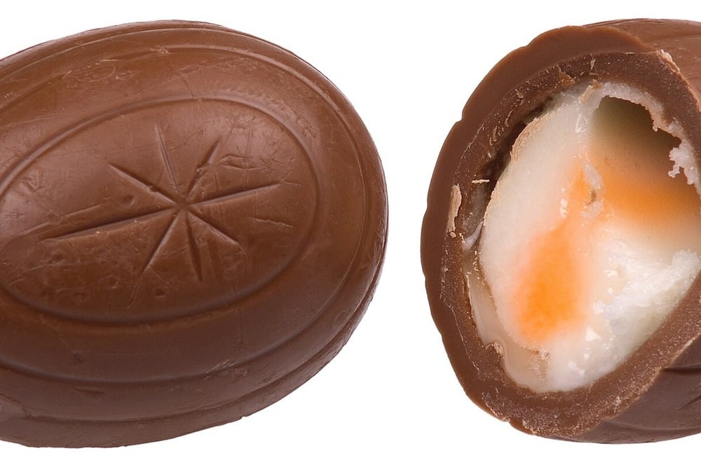 Close-up of a chocolate egg, one whole and one cut open to reveal a creamy white and orange filling inside.