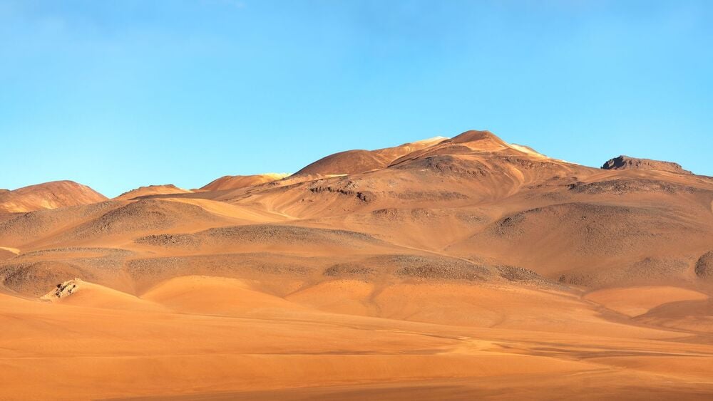 Rolling sandy hills and rocky outcrops under a clear blue sky in a desert landscape.