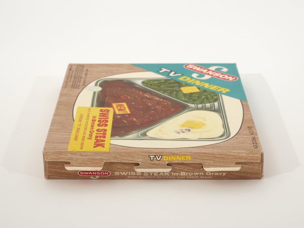 A vintage Swanson TV dinner box labeled “Swiss Steak in Brown Gravy” shows a meal with steak, mashed potatoes, and green beans, packaged in a divided tray on the cardboard box.
