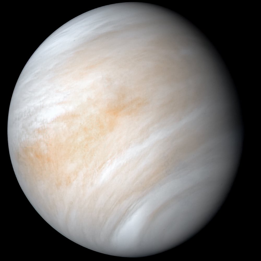 A view of planet Venus showing a smooth, pale surface with swirling white and beige cloud patterns, set against a black background.