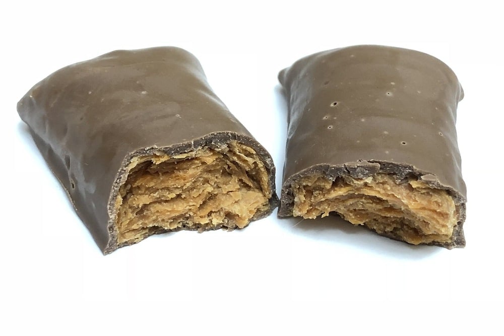 A chocolate-coated bar split in half, revealing multiple thin, flaky layers of a golden-brown filling inside. The outer layer is smooth and shiny.