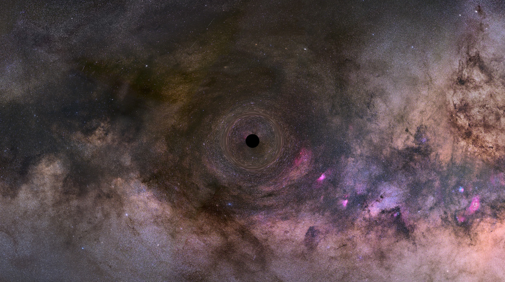 A black hole sits at the center of a colorful, swirling galaxy, with dark gas clouds and bright nebulae visible in the background.