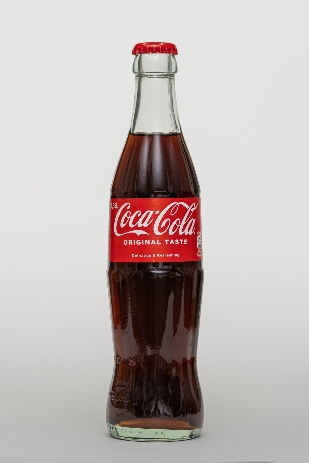 A classic glass bottle of Coca-Cola with a red cap and label reading “Coca-Cola Original Taste” against a plain white background.
