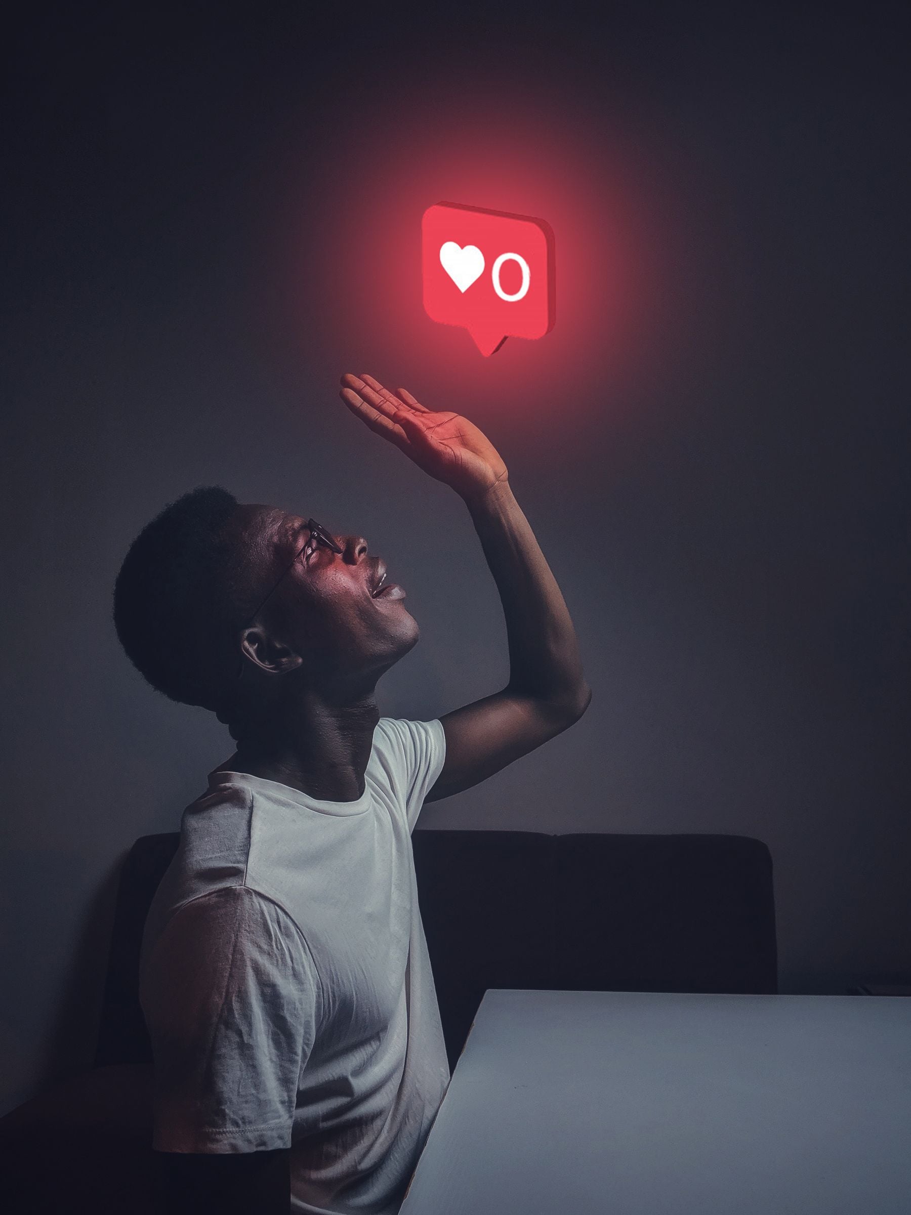 A person in a white shirt looks up and reaches toward a glowing red notification icon with a heart and zero, symbolizing no likes or approval, against a dark background.